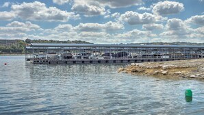 A waterfront pier with boats docked, a clear sky, and a distant shoreline. - Waterfront Lake Travis Home w/ Pool Access! (Leander)