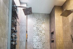 Une salle de bain avec un espace douche doté de plusieurs pommes de douche et d’un mur carrelé présentant différents motifs.
