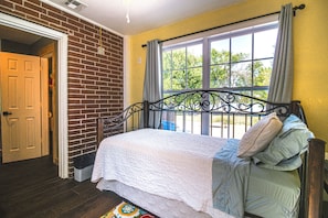 Une chambre avec un mur en briques, un lit recouvert d’une couette blanche et une fenêtre avec des rideaux.