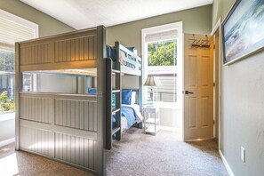 Une chambre avec un lit superposé, un bureau et une porte donnant sur une autre pièce.