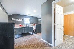 A bedroom with two beds, a wall-mounted air conditioner, a door with a pegboard, and a sign on the wall.