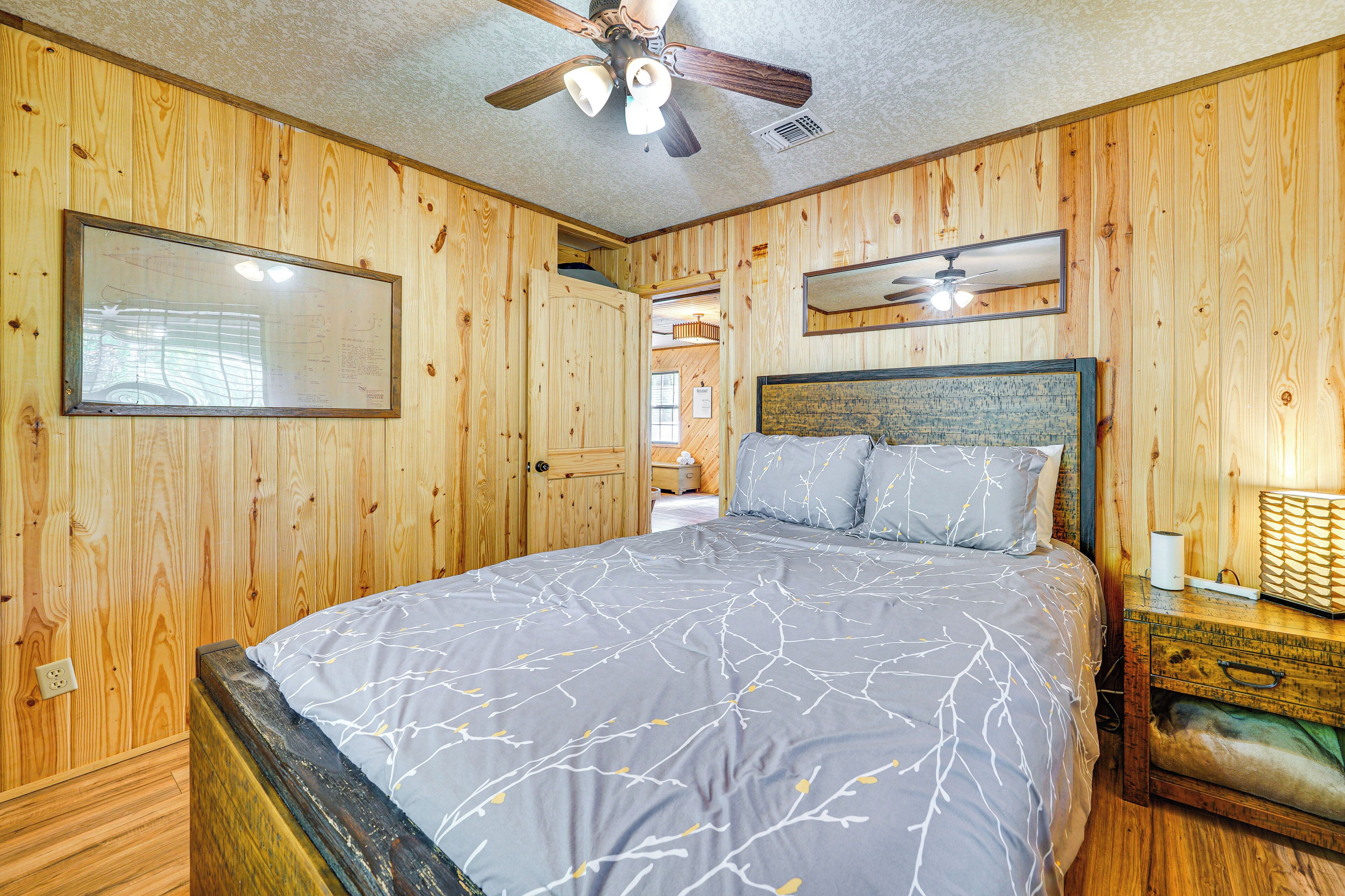 A wooden-paneled bedroom with a bed, a ceiling fan, and a nightstand.