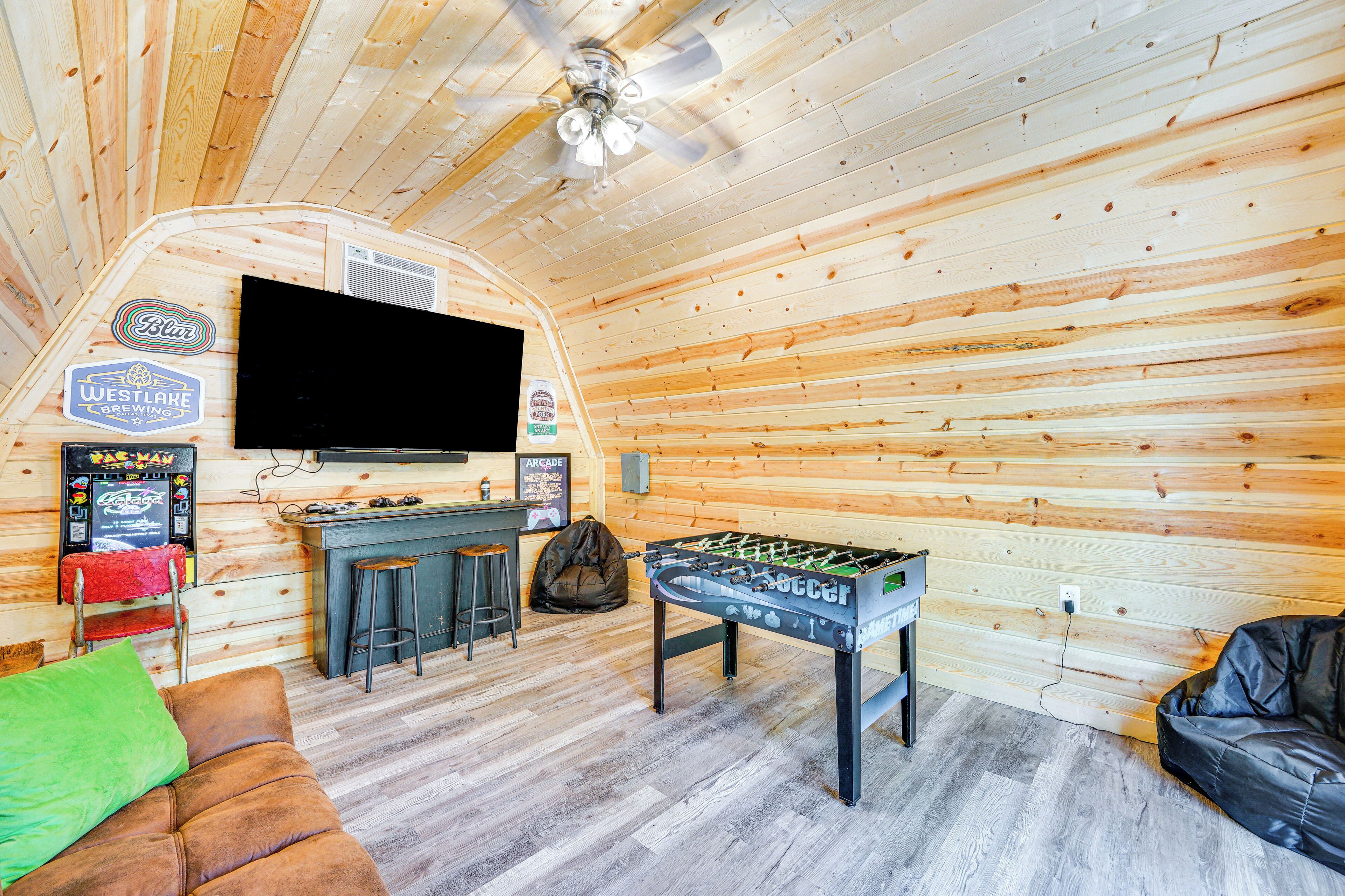 Une pièce chaleureuse aux murs en bois, avec un baby-foot, un téléviseur à écran plat et un coin bar équipé de tabourets.