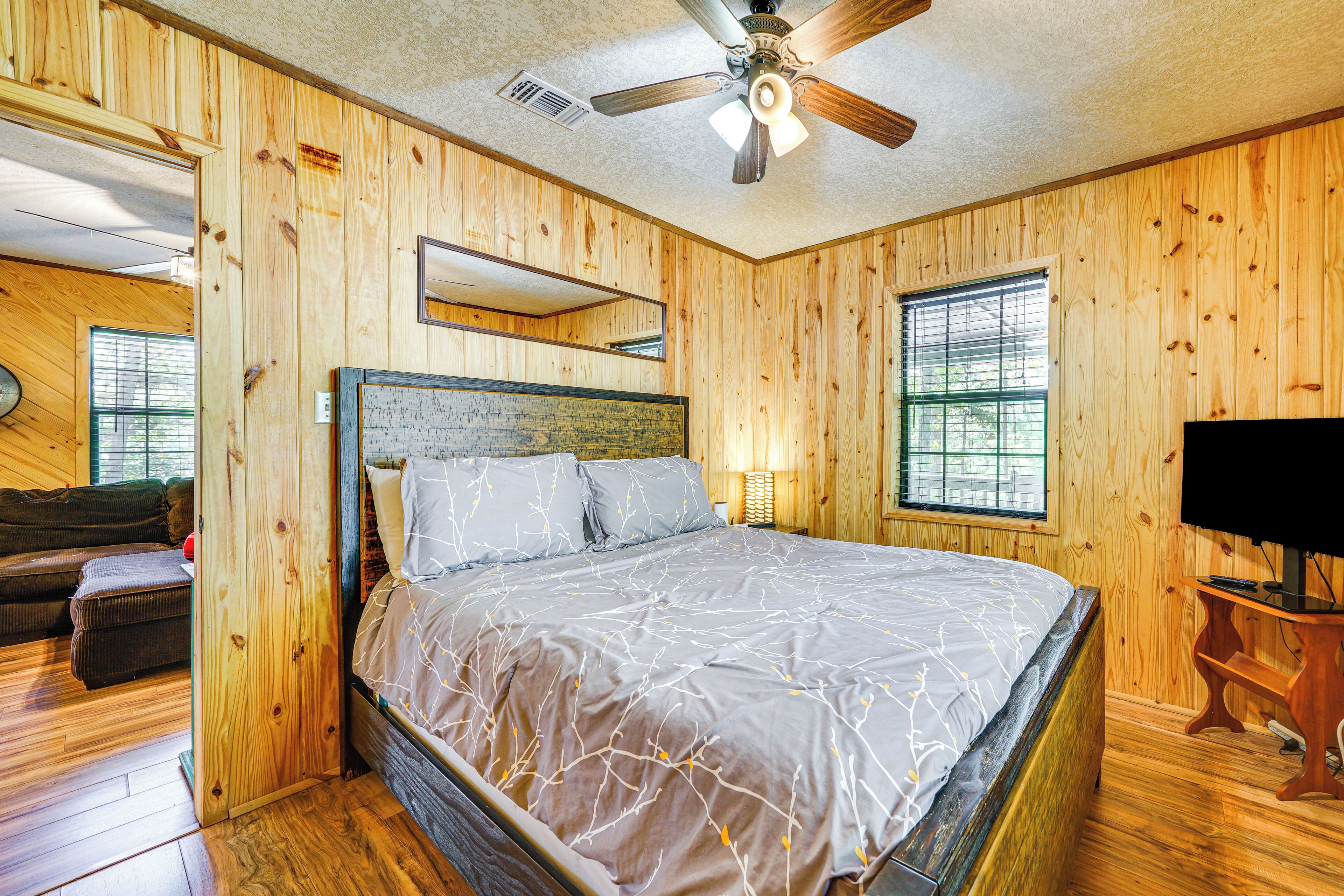 Une chambre aux murs lambrissés, avec un lit, un ventilateur de plafond et un téléviseur posé sur un meuble en bois.