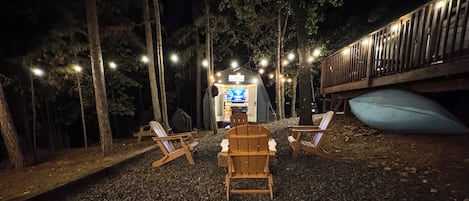 A nighttime outdoor seating area with two wooden chairs, a small table, and a tent-like structure with a sign.