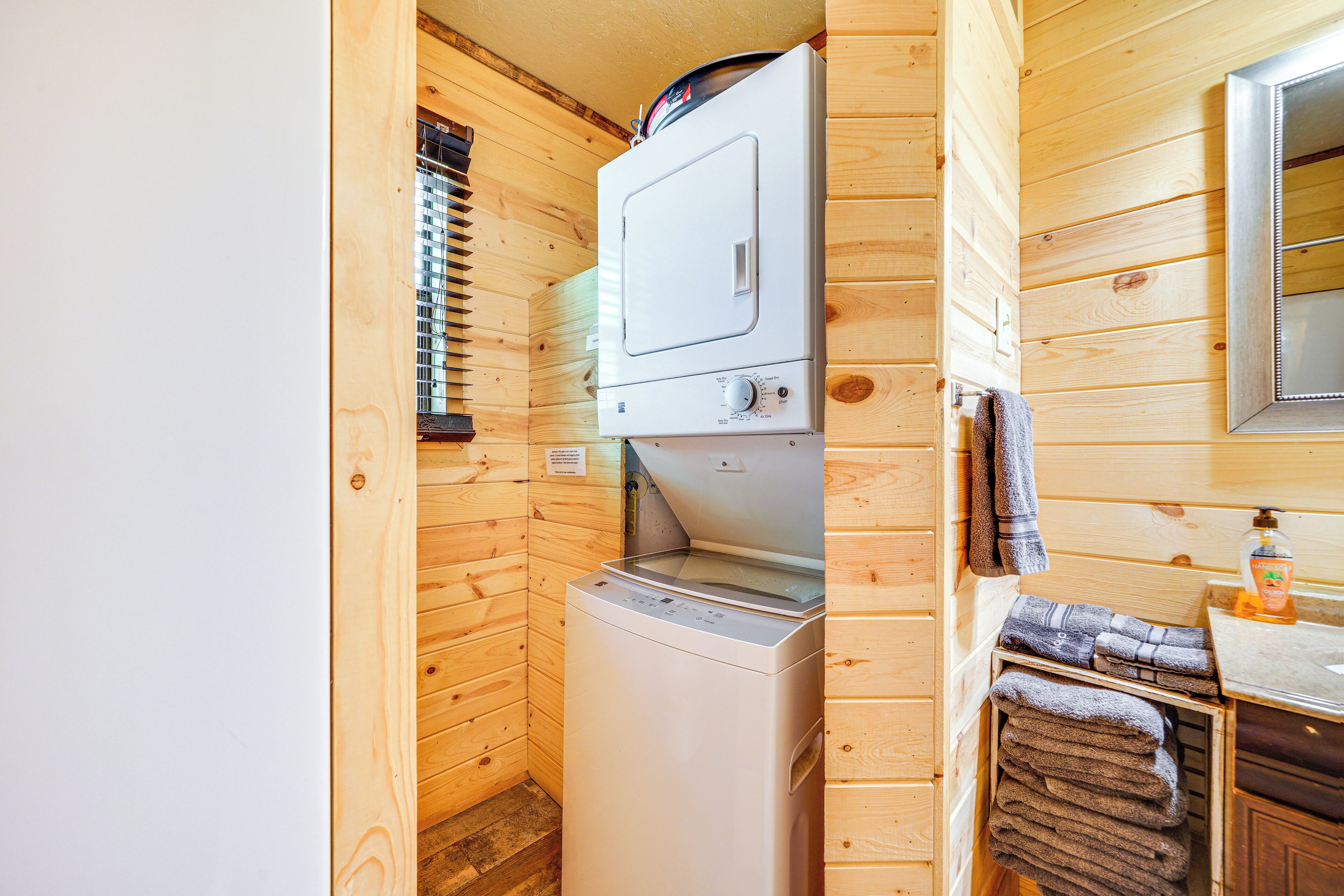 Una cabaña de madera pequeña con lavadora, un lavamanos y un espejo.