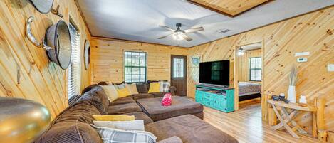 A cozy log cabin interior with a large sectional sofa, a television, and a wooden dining table.