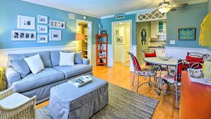 A living room with a grey sofa, a dining table with red chairs, and a kitchen in the background. - Condo w/ Pool Access: Walk to Shopping & Beach! (Naples)