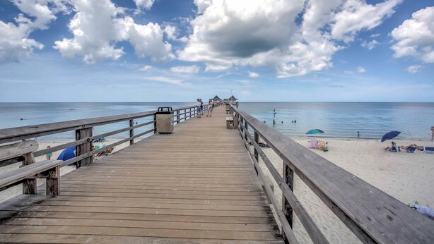 A wooden pier leading to a beach with umbrellas and people. - Condo w/ Pool Access: Walk to Shopping & Beach! (Naples)