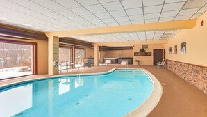 An indoor swimming pool with a tiled ceiling, a brick wall, and a door leading to another room.