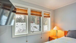 A bedroom with a bed, a nightstand with a lamp, and a window with blinds.