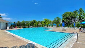 Ein rechteckiger Swimmingpool mit klarem, blauem Wasser, umgeben von einer Betonplattform und beschattet durch blaue Sonnenschirme.