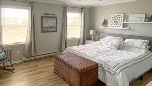 Ein Schlafzimmer mit einem Bett, einem Schaukelstuhl, einem Deckenventilator und einem Fenster mit Vorhängen.