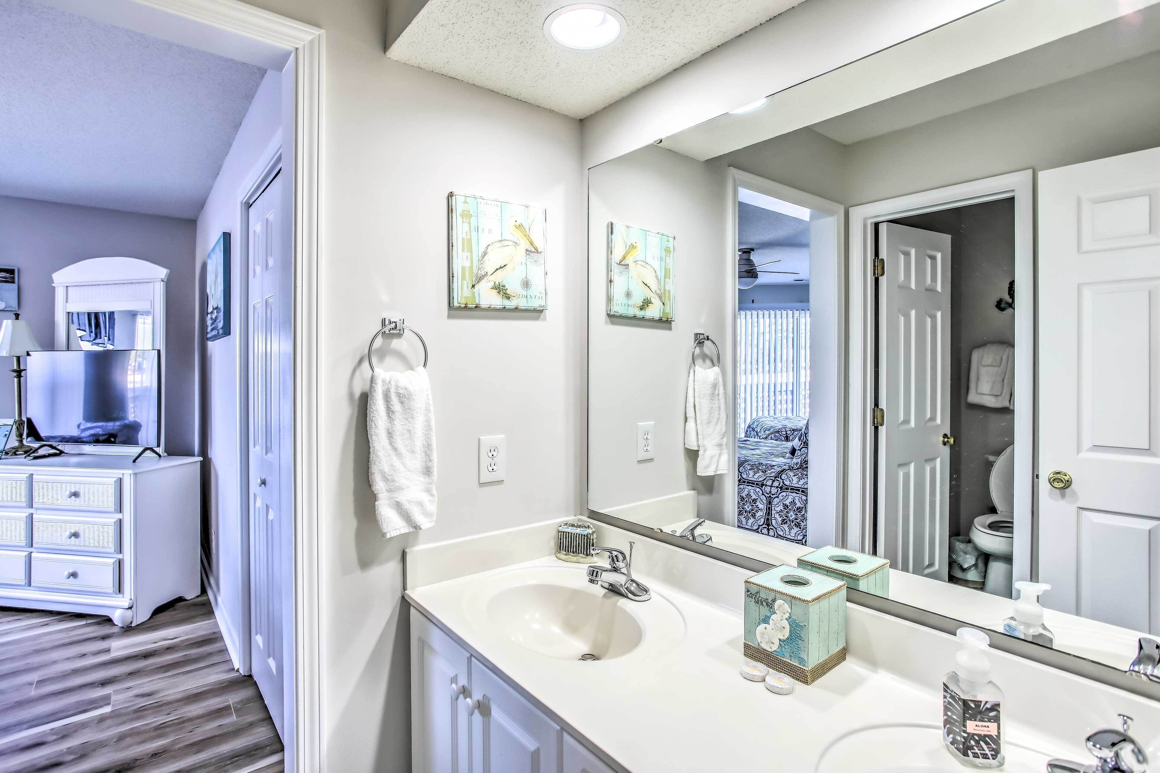 A bathroom with a large mirror, two wall-mounted light switches, a white sink, and a vanity with a mirror.