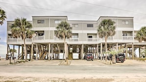 Ein Strandhotel mit mehreren Balkonen, Palmen und einem Sandstrand im Vordergrund.