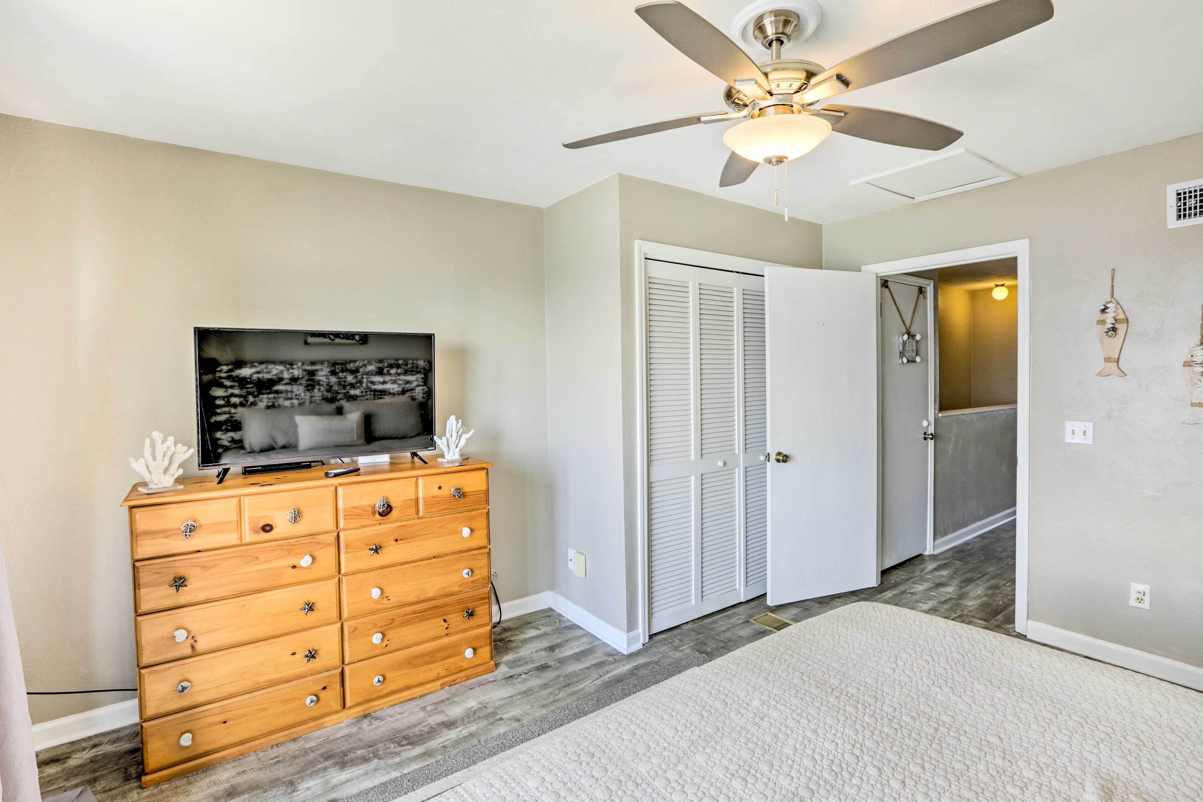 A bedroom with a wooden dresser, a ceiling fan, a television, and a closet.