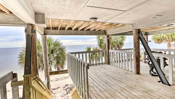 Eine Holzterrasse mit Geländer, die auf einen Strand und den Ozean blickt.