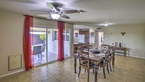 Un comedor con una mesa preparada para cuatro, un ventilador de techo y un puerta corrediza de vidrio que da a un patio exterior.