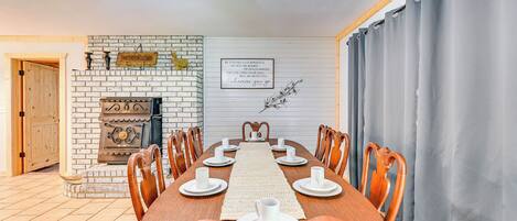 A dining room with a wooden table set for six, flanked by chairs, a brick fireplace, and a wall-mounted sign.