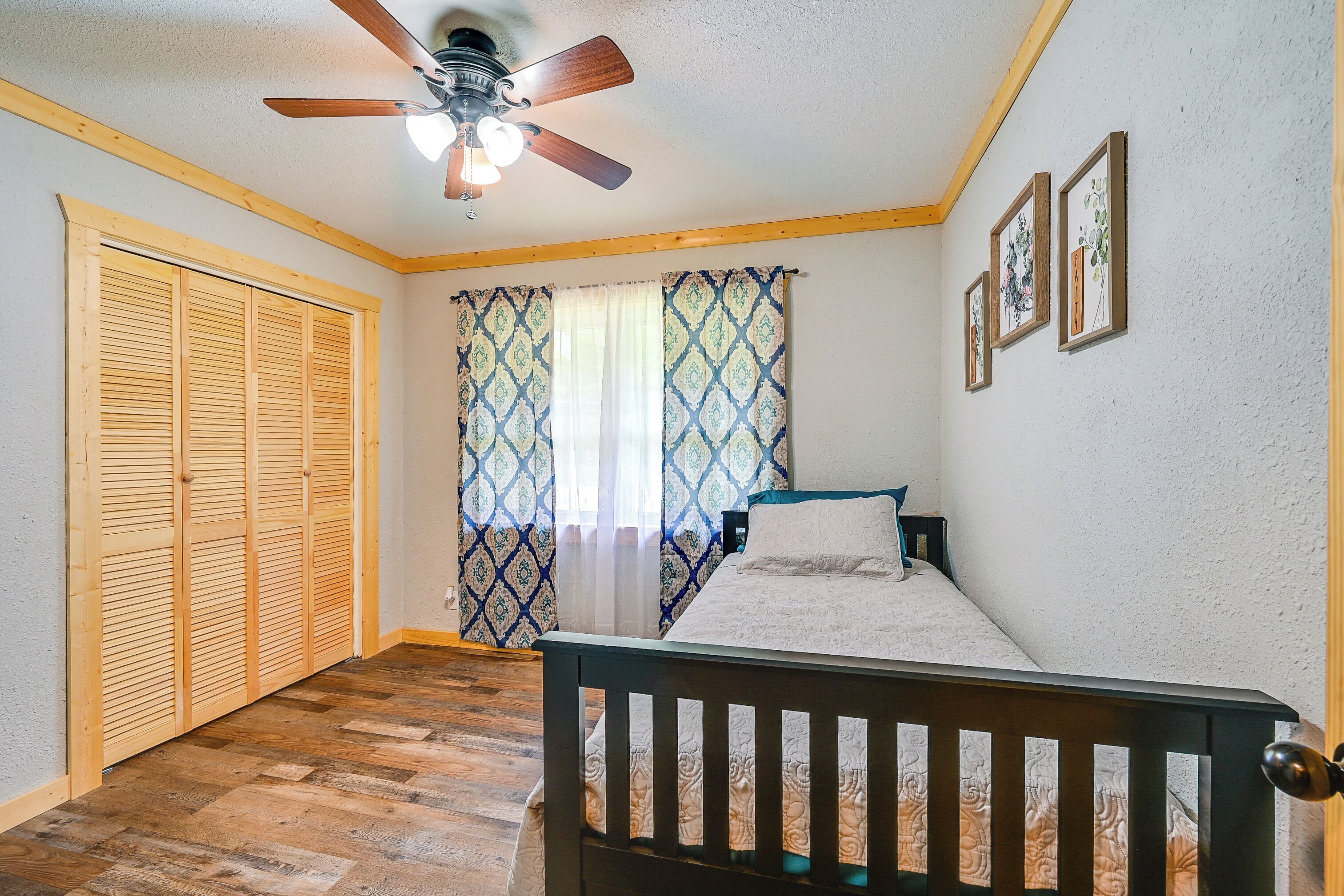 A bedroom with a wooden bed, a ceiling fan, a window with patterned curtains, and a wooden wardrobe.
