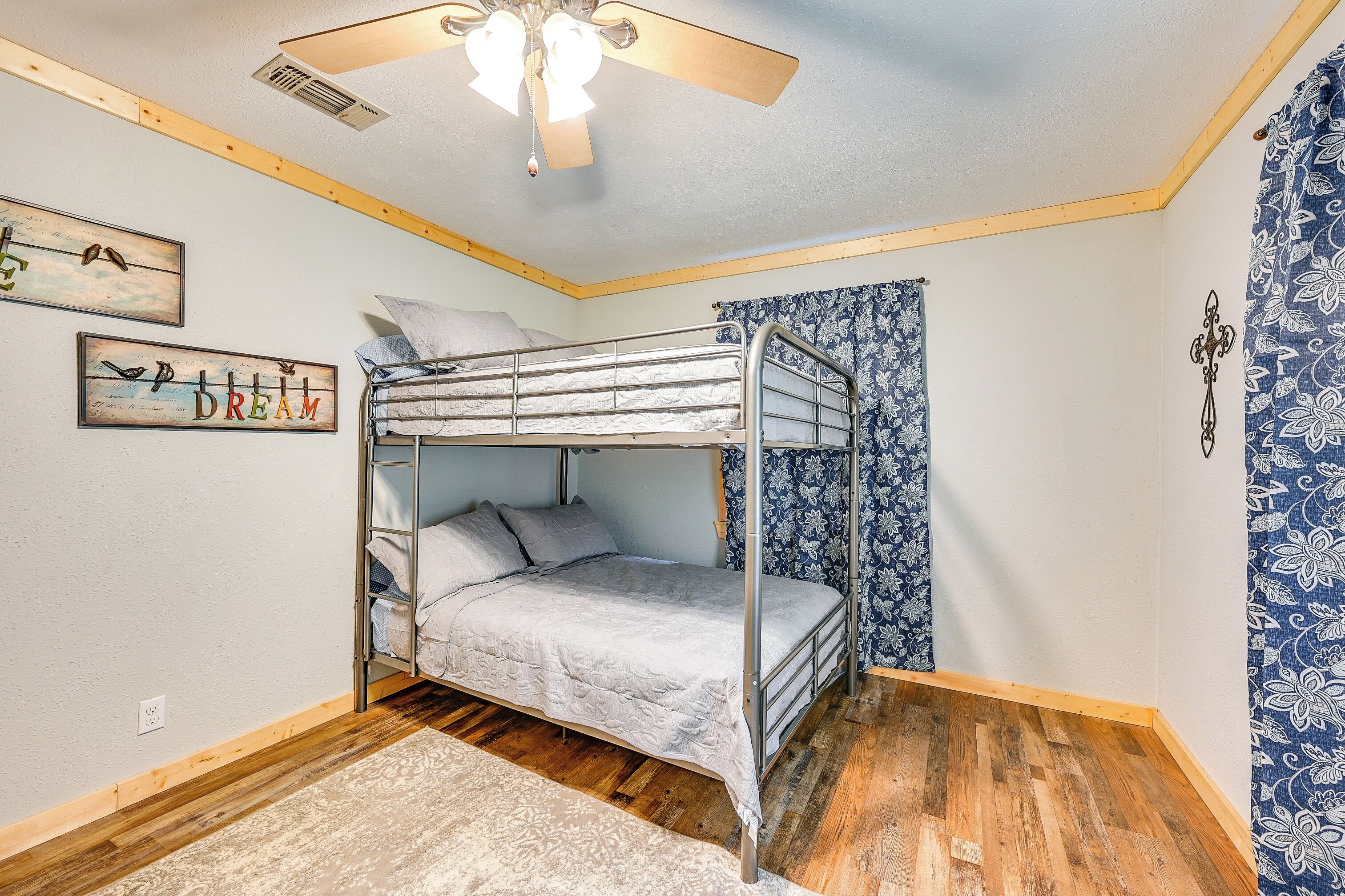 A bunk bed room with a ceiling fan, wooden flooring, and patterned wallpaper.