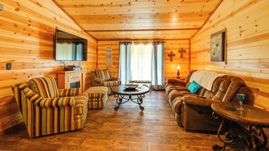 A cozy log cabin interior with striped armchairs, a sofa, a coffee table, and a fireplace.