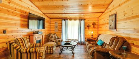 Accogliente interno di una baita in legno con poltrone a righe, un divano, un tavolino da caffè e un caminetto.