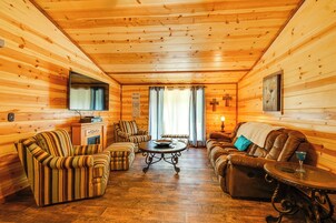 Un interior acogedor de cabaña de madera con sillones a rayas, un sofá, una mesa de centro y una chimenea.