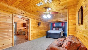 A log cabin room with a bed, a sofa, a ceiling fan, and a wooden wall.