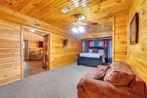 Habitación tipo cabaña de madera con cama, sofá, ventilador de techo y pared de madera.