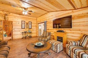 Interior acogedor de una cabaña de madera con chimenea, sillones a rayas, una mesa de centro redonda y una cornamenta de venado.