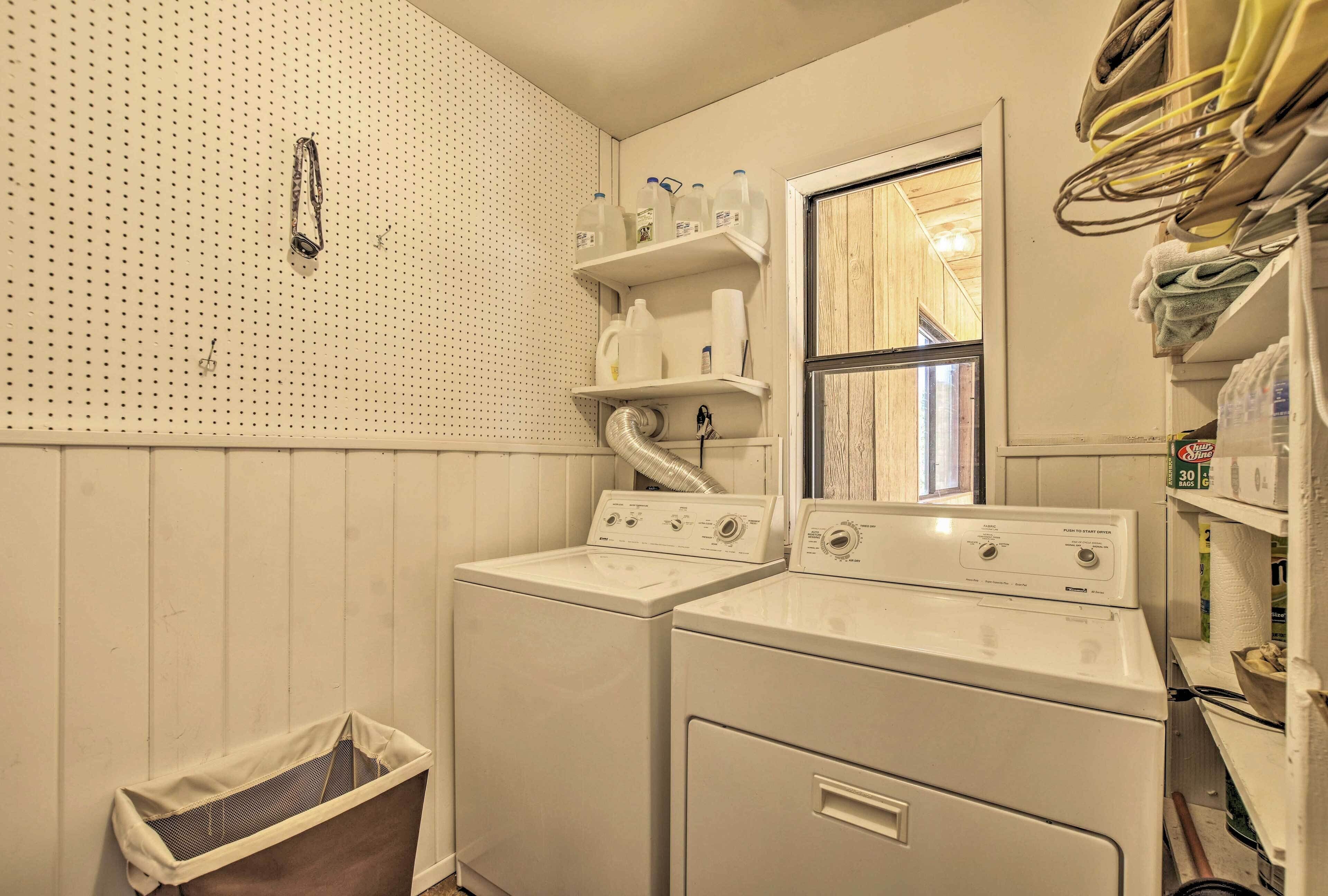 A laundry room with two stacked washers and dryers, a pegboard wall, and shelves with laundry supplies.