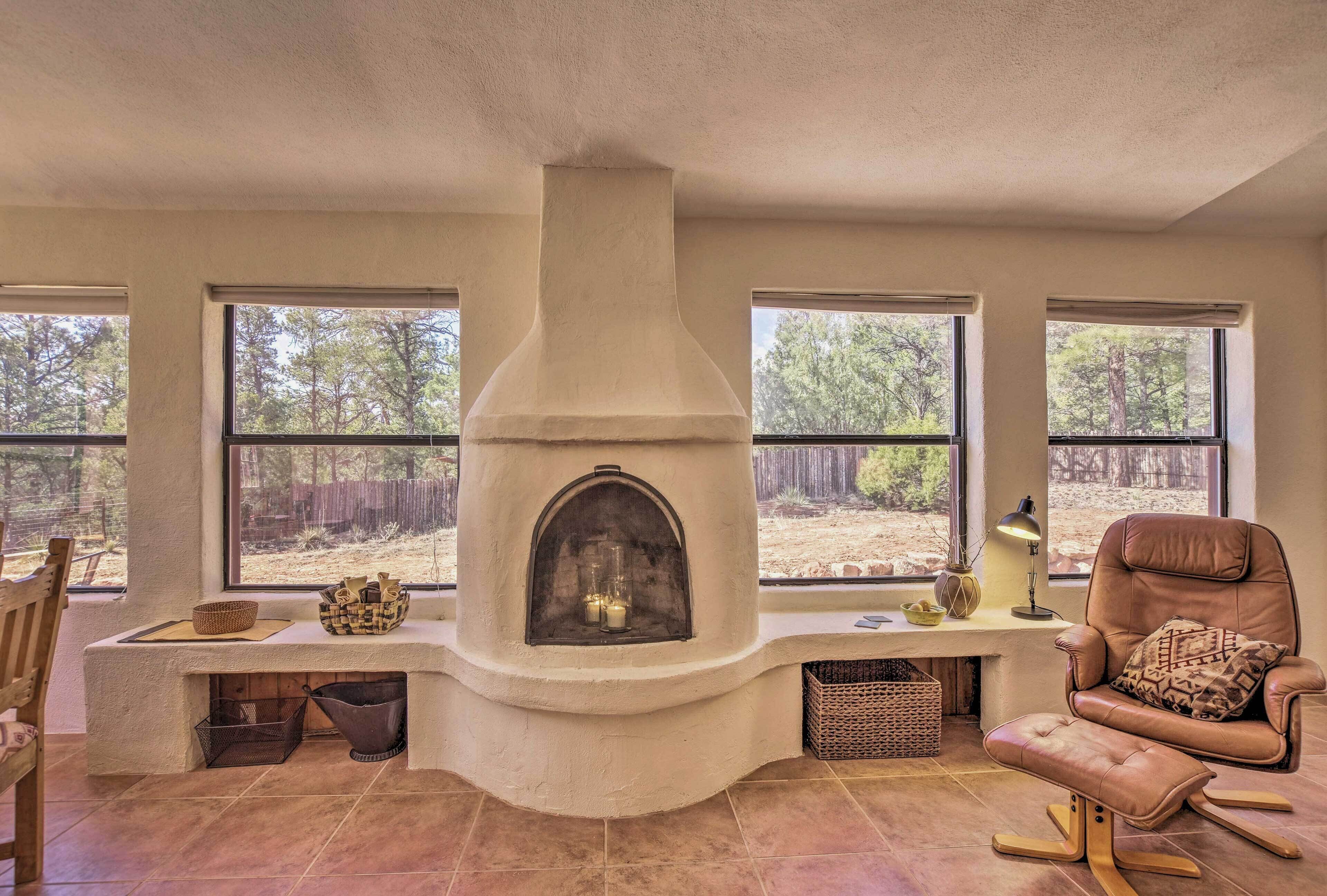 A cozy living room with a fireplace, large windows, a comfortable chair, and a dining area.