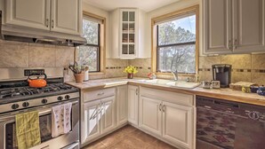 A kitchen with white cabinets, a stove, oven, and dishwasher. There are windows, a sink, and a countertop with various items. - Artist's Retreat w/ Pecos National Park Views! (Rowe)