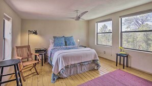 A bedroom with a bed, a chair, a table, a standing lamp, and large windows. - Artist's Retreat w/ Pecos National Park Views! (Rowe)