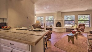 A spacious living area with a fireplace, large windows, and a kitchen counter. - Artist's Retreat w/ Pecos National Park Views! (Rowe)