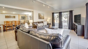 Un salon moderne avec un canapé en cuir, un coin repas avec des chaises en bois, un téléviseur à écran plat et de grandes fenêtres avec des rideaux.
