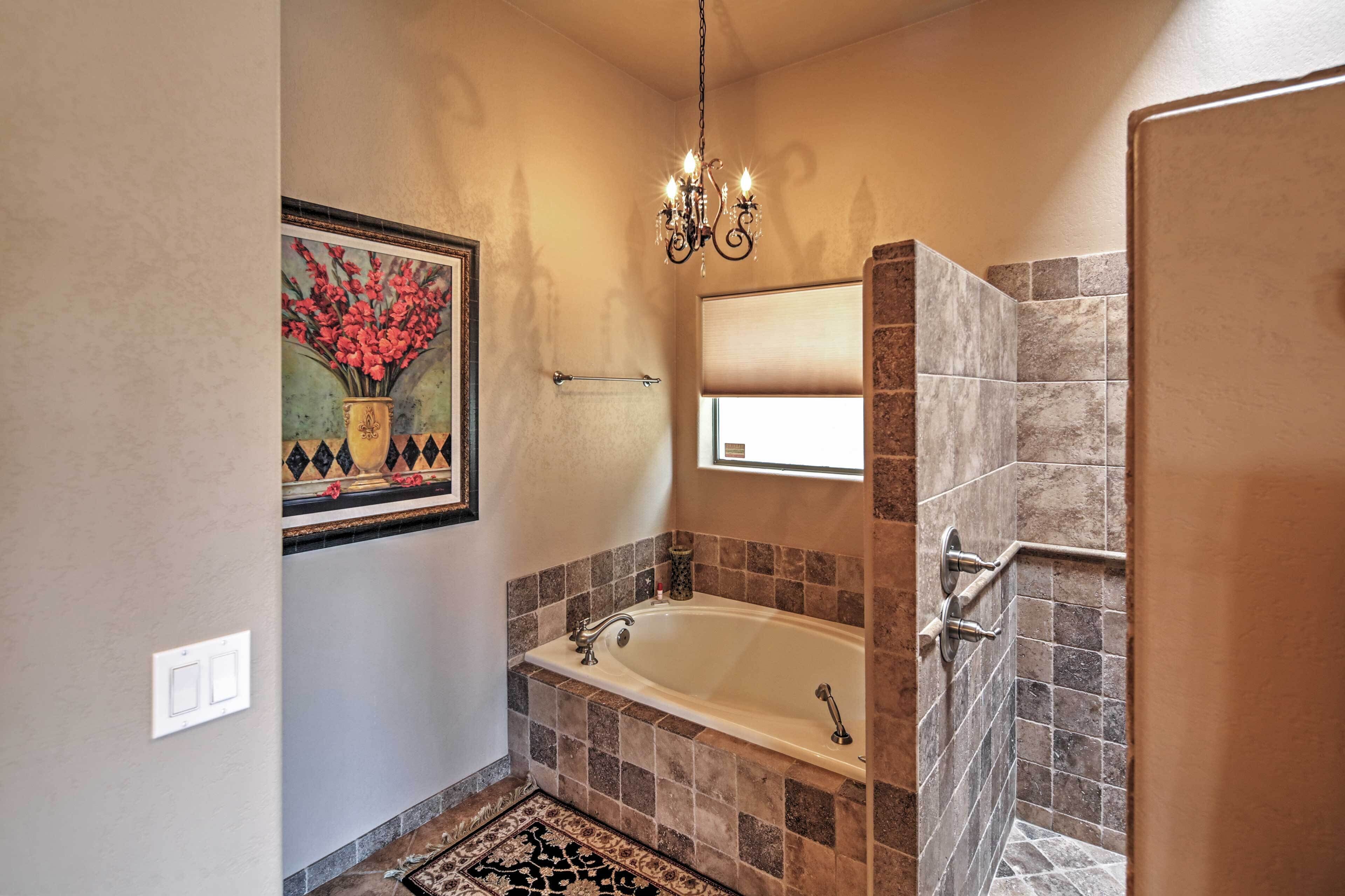 Une salle de bain avec une baignoire, une douche, un lustre et un tableau encadré au mur.