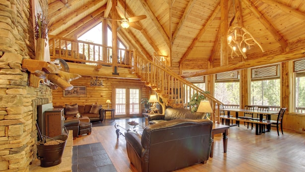 A spacious log cabin interior with a stone fireplace, leather furniture, a dining area, and large windows. - Lakeside Cabin on 2 Acres w/ Fire Pit + Hot Tub! (Lakeside)