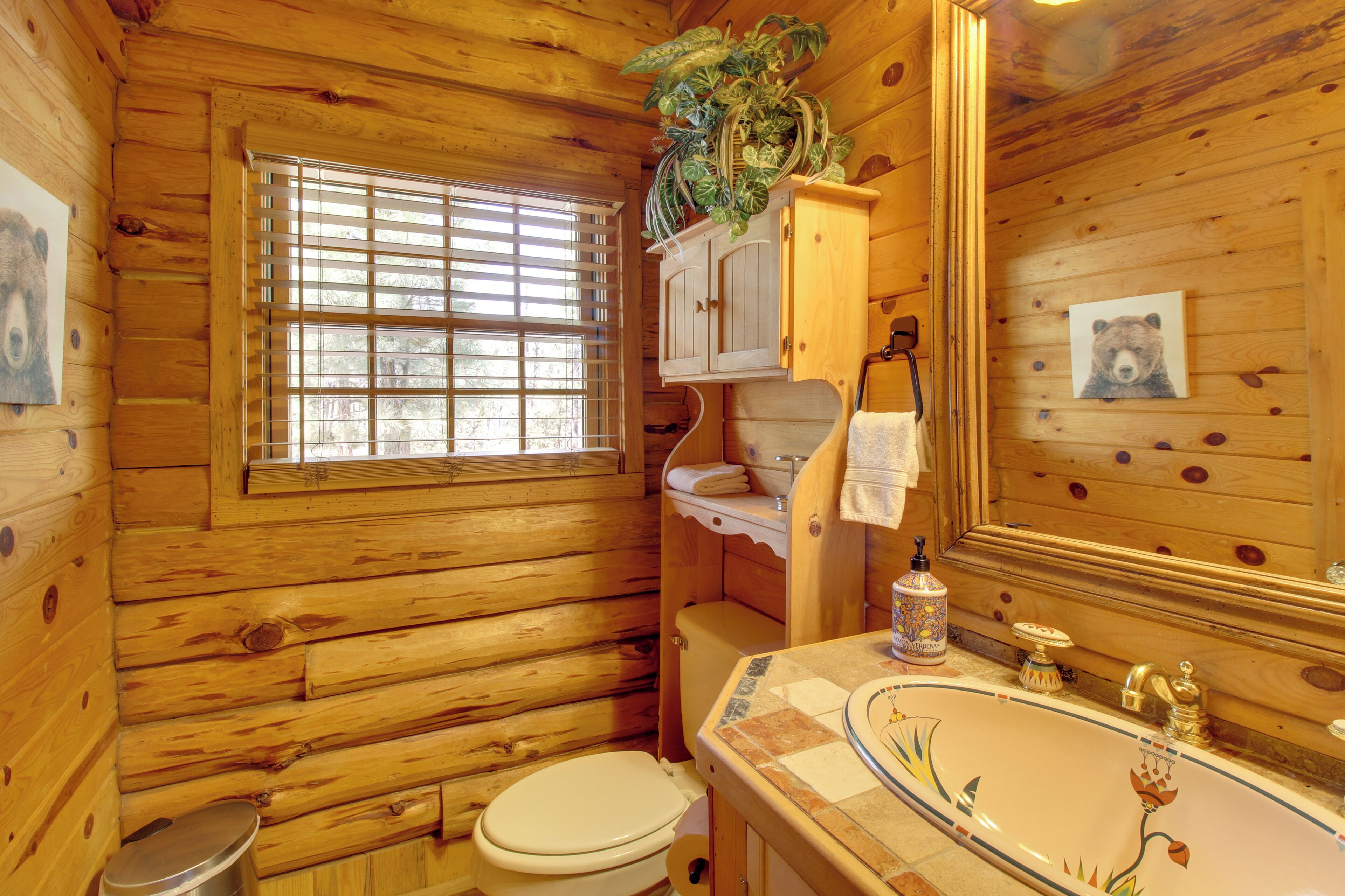A wooden cabin bathroom with a toilet, sink, and window with blinds.