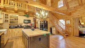 A spacious log cabin with a large kitchen area, wooden floors, and a staircase leading to an upper level. - Lakeside Cabin on 2 Acres w/ Fire Pit + Hot Tub! (Lakeside)