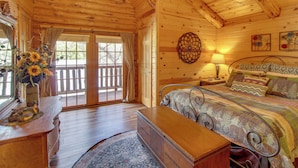 A wooden cabin interior with a bed, a nightstand, a dresser, and a large window. - Lakeside Cabin on 2 Acres w/ Fire Pit + Hot Tub! (Lakeside)