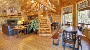 A wooden interior with a fireplace, a staircase, and a dining area. - Lakeside Cabin on 2 Acres w/ Fire Pit + Hot Tub! (Lakeside)