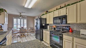A kitchen with white cabinets, a black refrigerator, a stove, and a microwave. There is a dining area with a table and chairs. - Golf, Hike & Suntan: Mesa Family Home w/ Yard (Mesa)