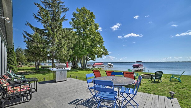 A deck with a table and chairs, overlooking a lake with boats and a dock.