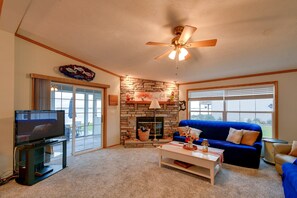 Una sala de estar con televisor, chimenea, sofá azul y ventilador de techo.