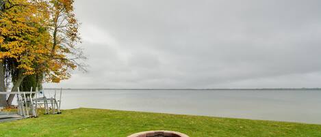 Een gazon met een vuurkorf van steen en een waterpartij op de achtergrond.