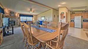 A spacious living room with a fireplace, dining area with wooden chairs, and a kitchen with wooden cabinets and appliances.