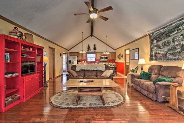A spacious living room with a wooden coffee table, red shelving unit, and a ceiling fan. - Firefly Cove - 3 Mi to Parkway & National Park! (Sevierville)