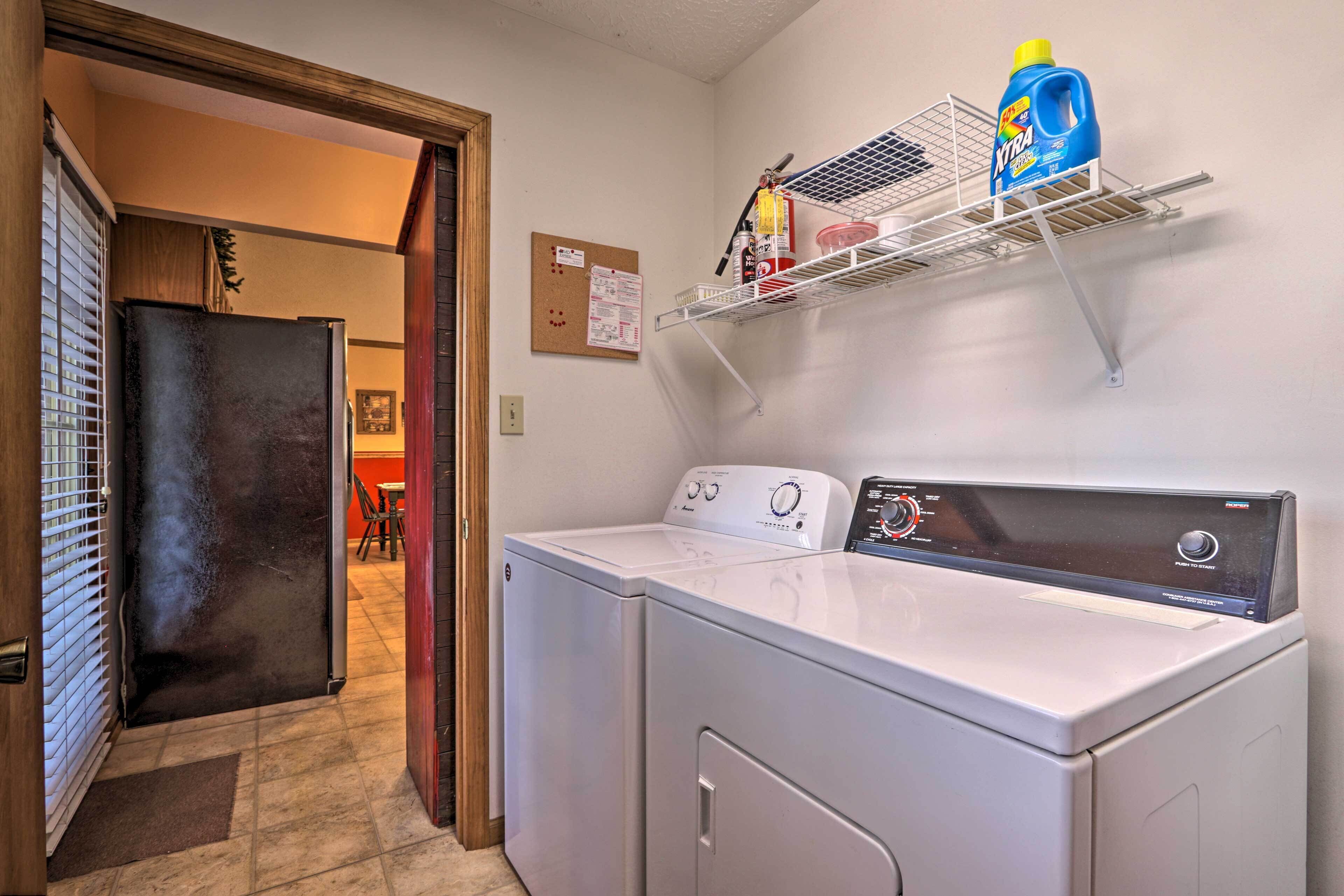 A laundry area with a washing machine and dryer, a shelf with cleaning supplies, and a bulletin board on the wall.